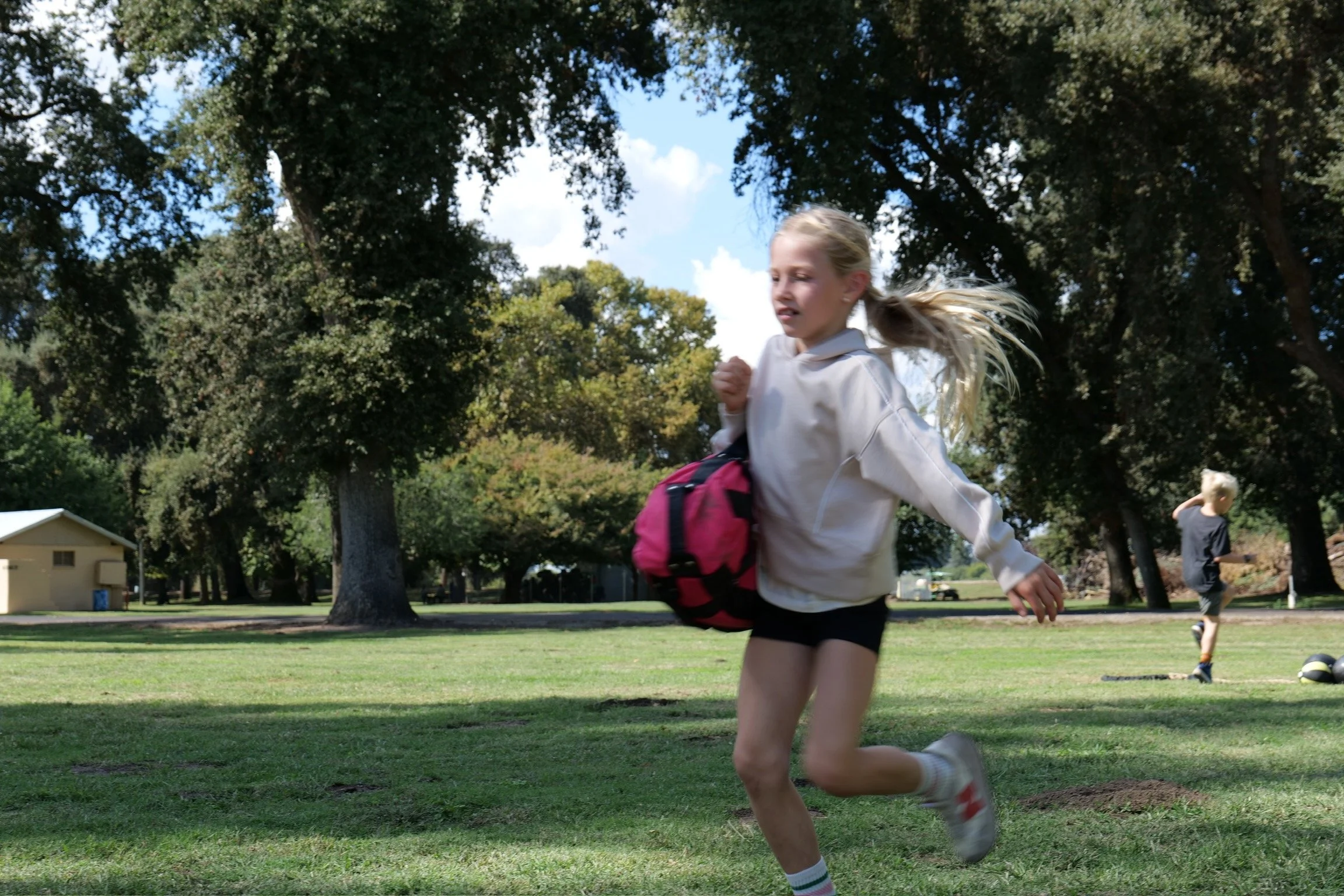 Children running with exercise sandbags on grass at a Fit Visalia session
